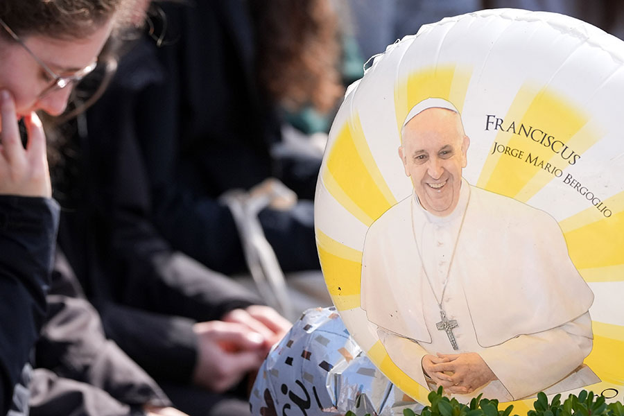 woman prays, a balloon of Pope Francis beside her